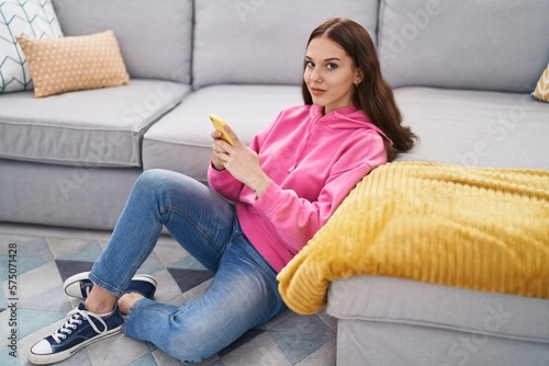 Young woman using smartphone sitting on floor at home