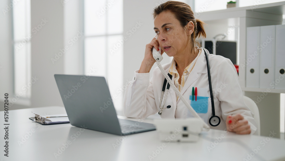 Middle age hispanic woman wearing doctor uniform talking on the telephone at clinic Middle age hispanic woman wearing doctor uniform talking on the telephone at clinic