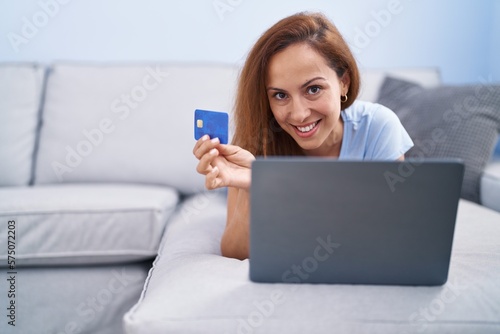Young woman using laptop and credit card lying on sofa at home