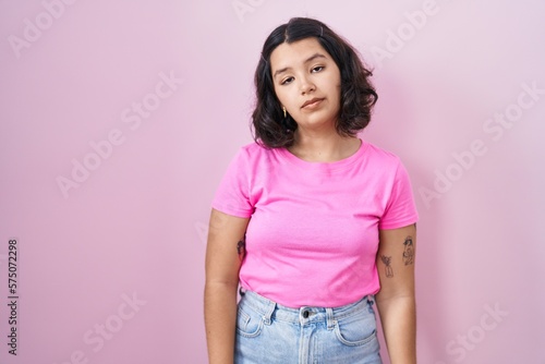 Young hispanic woman standing over pink background looking sleepy and tired, exhausted for fatigue and hangover, lazy eyes in the morning.