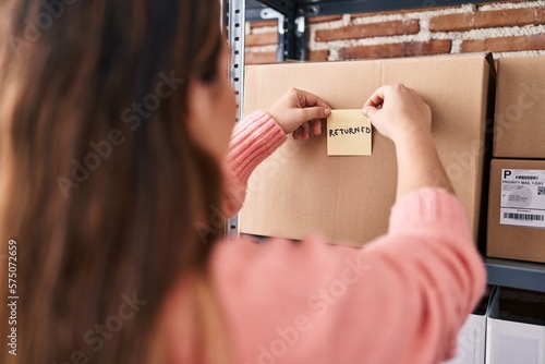 Young beautiful hispanic woman ecommerce business worker putting returned reminder paper on package at office