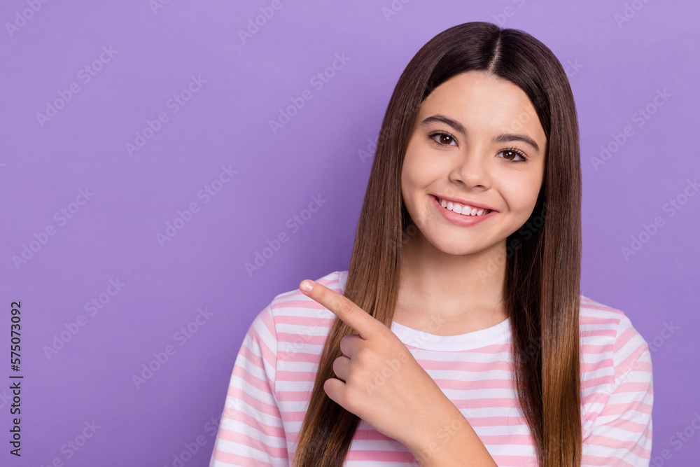 Photo of positive lovely girl toothy smile indicate finger empty space isolated on violet color background Photo of positive lovely girl toothy smile indicate finger empty space isolated on violet color background