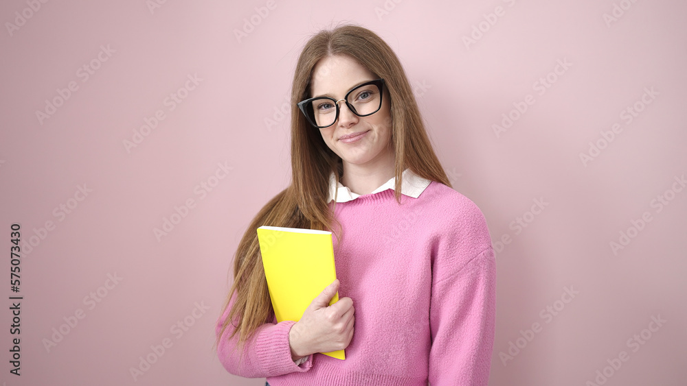Young blonde woman smiling confident holding book over isolated pink background Young blonde woman smiling confident holding book over isolated pink background