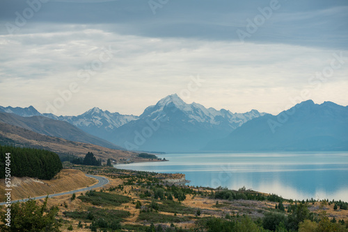 Panorama Straße an einem See mit schneebedeckten Bergen und türkisem Wasser.