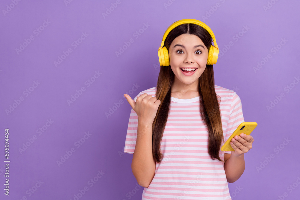 Photo of adorable excited lady wear striped t-shirt listening music modern device thumb empty space isolated violet color background Photo of adorable excited lady wear striped t-shirt listening music modern device thumb empty space isolated violet color background