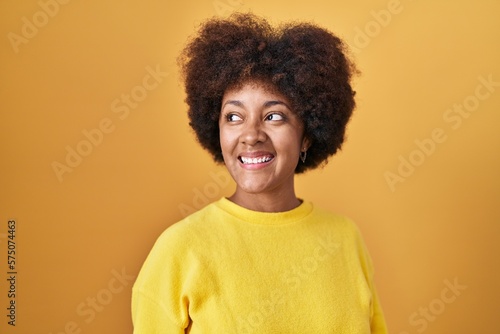Young african american woman standing over yellow background looking away to side with smile on face, natural expression. laughing confident. © Krakenimages.com
