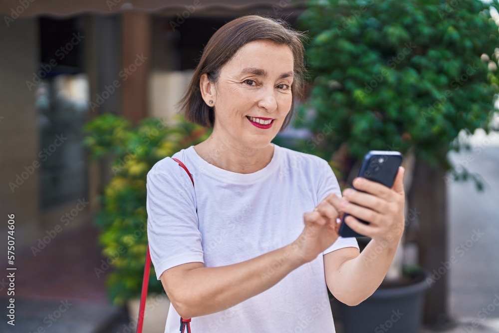 Middle age woman smiling confident using smartphone at street