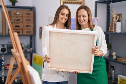 Two women artists smiling confident holding draw canvas at art studio