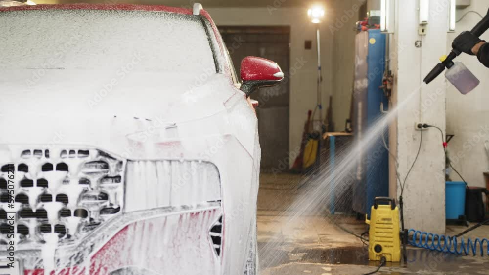 Manual car washing concept. Young man worker cleaning modern red car