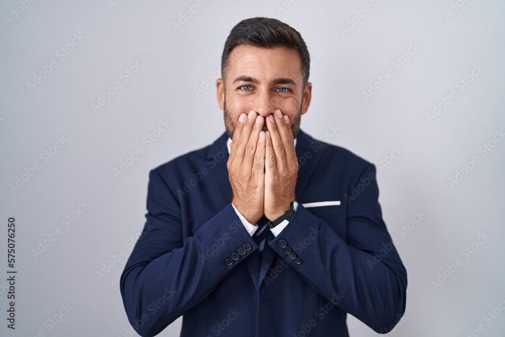 Handsome hispanic man wearing suit and tie laughing and embarrassed giggle covering mouth with hands, gossip and scandal concept Handsome hispanic man wearing suit and tie laughing and embarrassed giggle covering mouth with hands, gossip and scandal concept