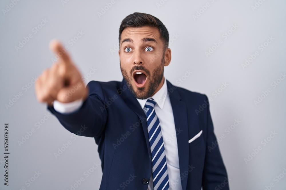 Handsome hispanic man wearing suit and tie pointing with finger surprised ahead, open mouth amazed expression, something on the front Handsome hispanic man wearing suit and tie pointing with finger surprised ahead, open mouth amazed expression, something on the front