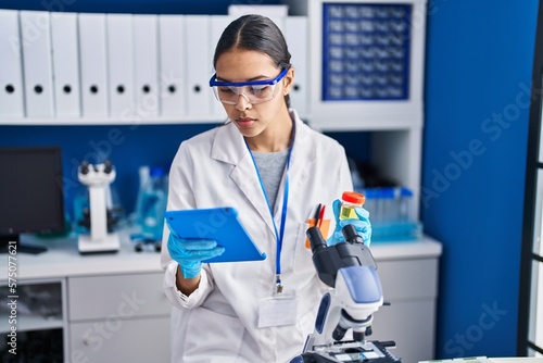 Young african american woman scientist analysing urine test tube using touchpad at laboratory