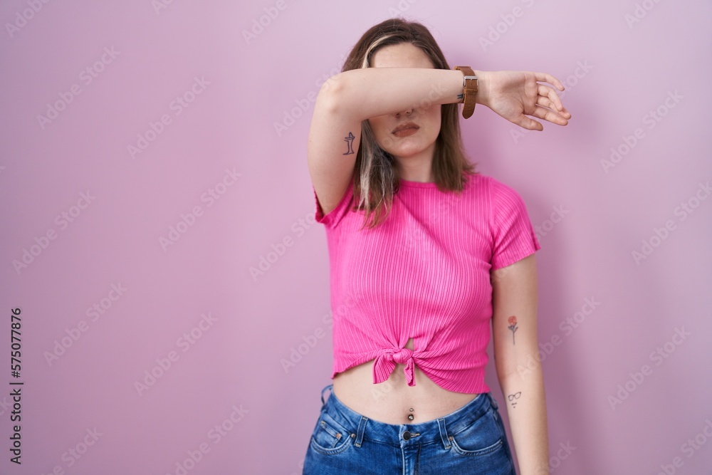 Blonde caucasian woman standing over pink background covering eyes with arm, looking serious and sad. sightless, hiding and rejection concept Blonde caucasian woman standing over pink background covering eyes with arm, looking serious and sad. sightless, hiding and rejection concept
