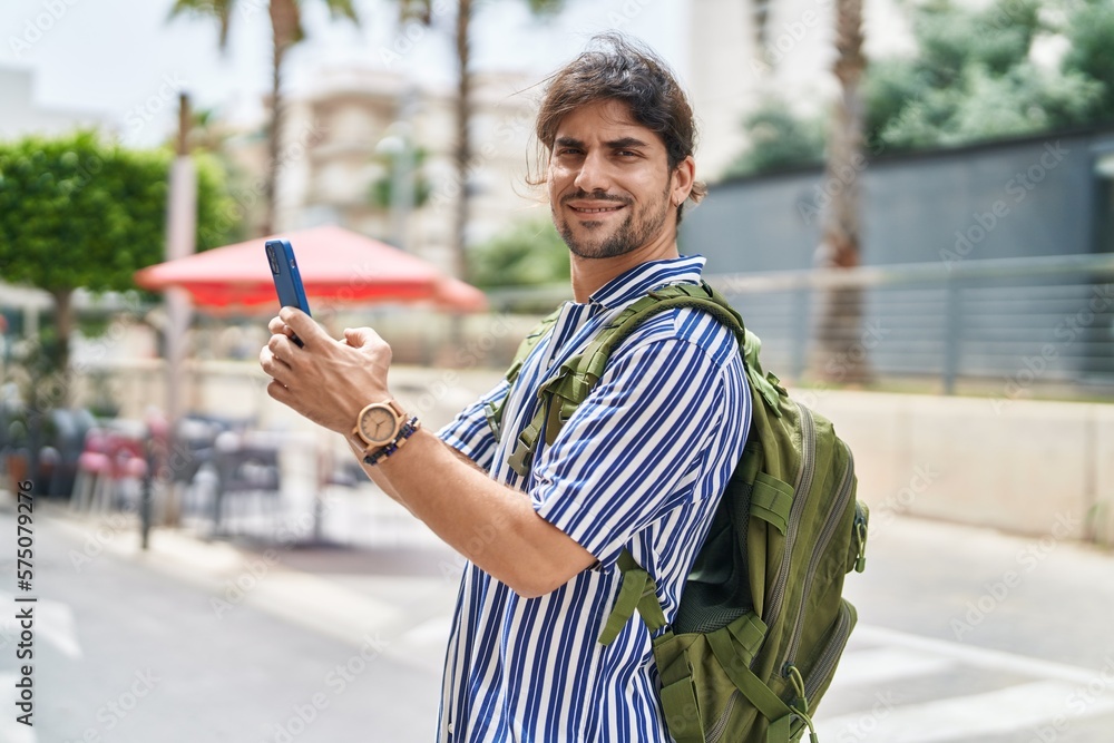 Young hispanic man tourist wearing backpack using smartphone at street Young hispanic man tourist wearing backpack using smartphone at street