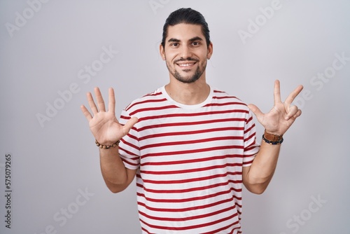 Hispanic man with long hair standing over isolated background showing and pointing up with fingers number eight while smiling confident and happy.