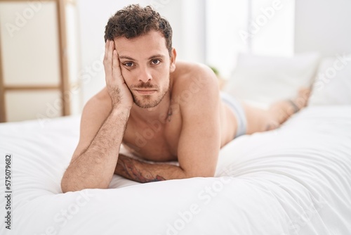 Young hispanic man lying on bed with relaxed expression at bedroom