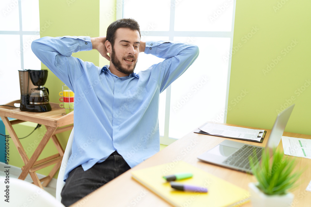 Young hispanic man business worker relaxed with hands on head at office