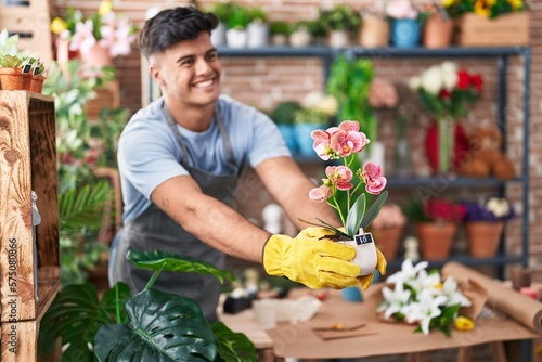 Young hispanic man florist smiling confident holding plant at flower shop