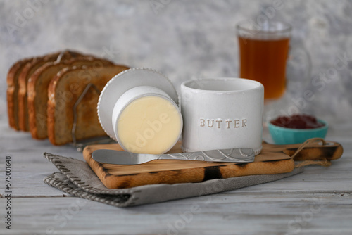 Vintage butter bell and silver knife on wood cutting board,  toast bread, tea and strawberry jam. Rustic white background.