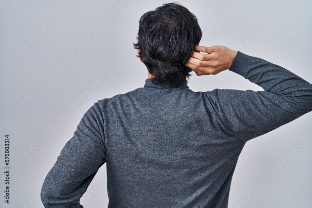 Handsome latin man standing over isolated background backwards thinking about doubt with hand on head Handsome latin man standing over isolated background backwards thinking about doubt with hand on head