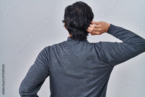 Handsome latin man standing over isolated background backwards thinking about doubt with hand on head