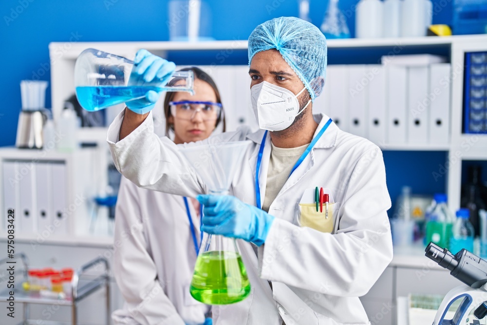 Man and woman scientists pouring liquid on test tube at laboratory Man and woman scientists pouring liquid on test tube at laboratory