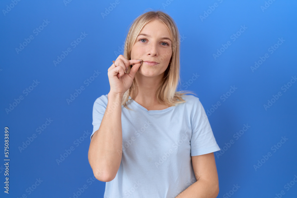 Young caucasian woman wearing casual blue t shirt mouth and lips shut as zip with fingers. secret and silent, taboo talking Young caucasian woman wearing casual blue t shirt mouth and lips shut as zip with fingers. secret and silent, taboo talking