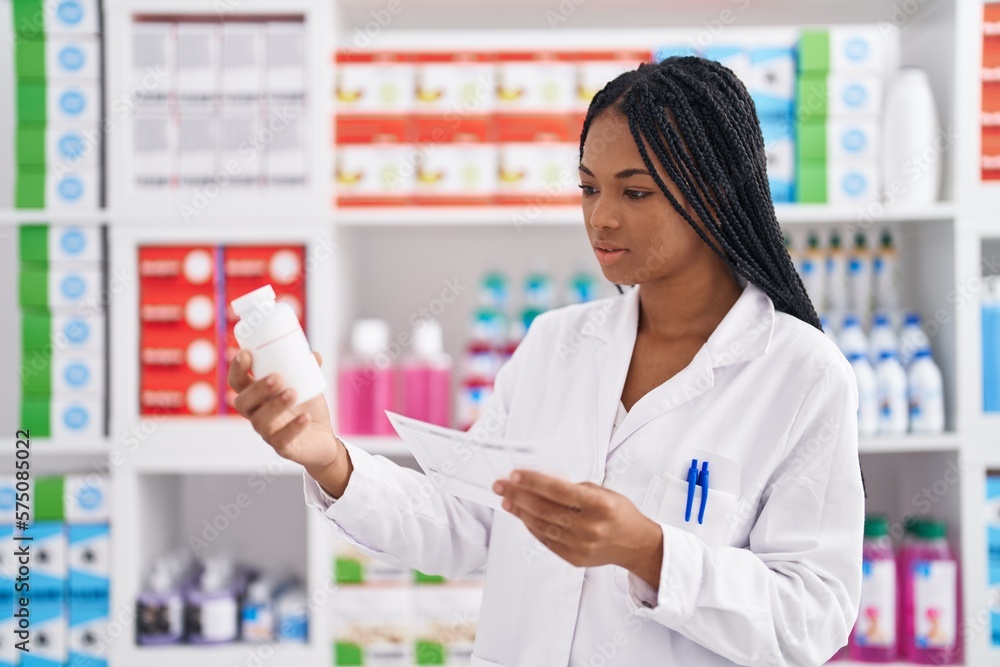 African american woman pharmacist holding pills bottle reading prescription at pharmacy