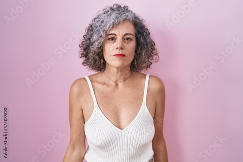 Middle age woman with grey hair standing over pink background relaxed with serious expression on face. simple and natural looking at the camera.