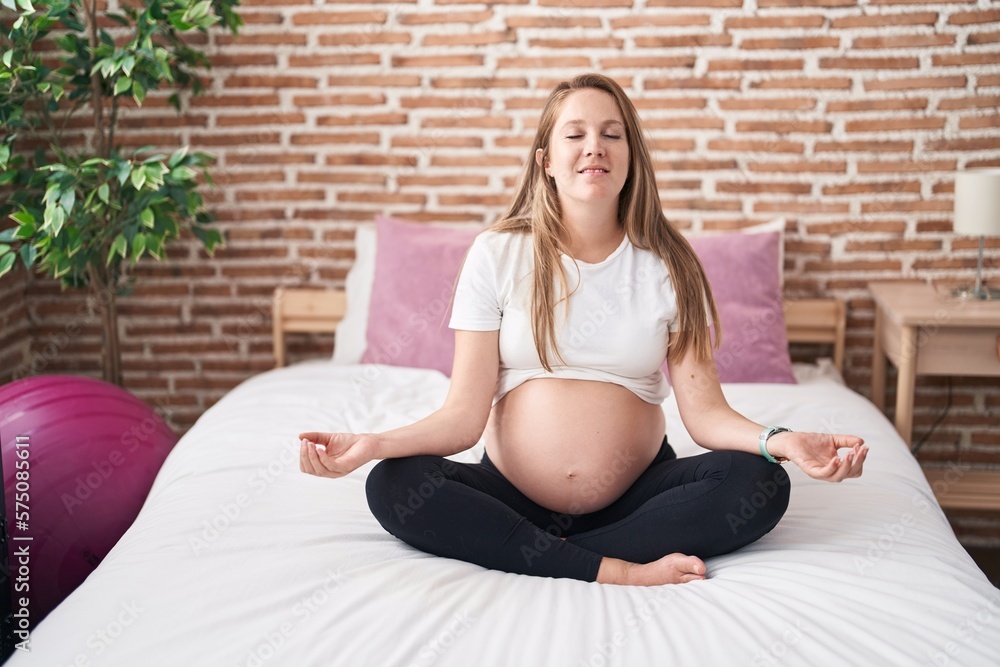 Young pregnant woman doing yoga exercise sitting on bed at bedroom