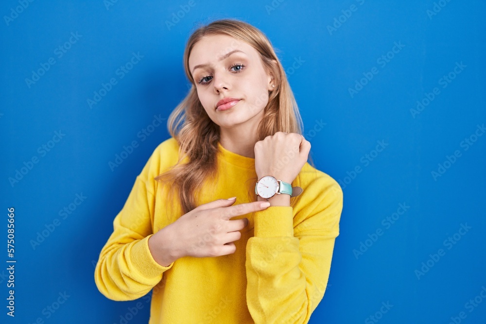 Young caucasian woman standing over blue background in hurry pointing to watch time, impatience, looking at the camera with relaxed expression Young caucasian woman standing over blue background in hurry pointing to watch time, impatience, looking at the camera with relaxed expression