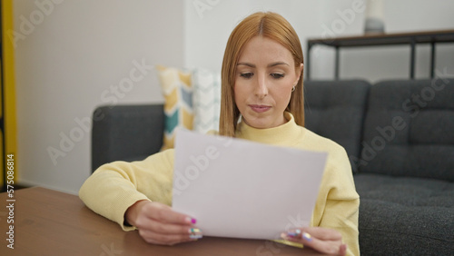 Young blonde woman reading document sitting on floor at home