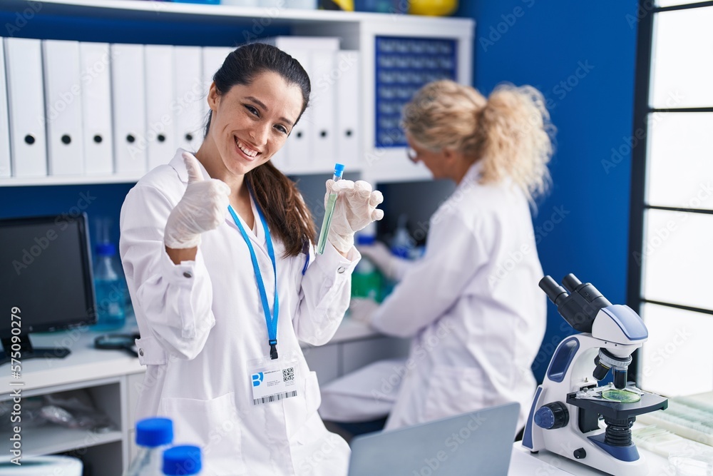 Young hispanic woman working at scientist laboratory smiling happy and positive, thumb up doing excellent and approval sign Young hispanic woman working at scientist laboratory smiling happy and positive, thumb up doing excellent and approval sign