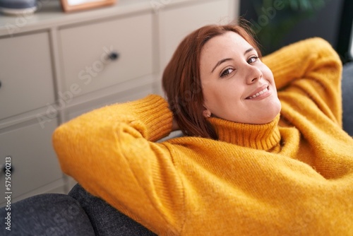 Young beautiful plus size woman relaxed with hands on head sitting on sofa at home