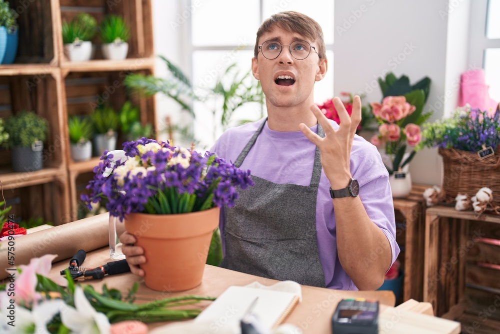 Caucasian blond man working at florist shop crazy and mad shouting and yelling with aggressive expression and arms raised. frustration concept.