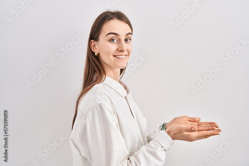 Young caucasian woman standing over isolated background pointing aside with hands open palms showing copy space  presenting advertisement smiling excited happy