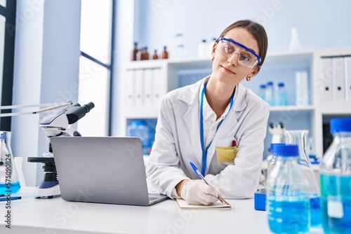 Young caucasian woman scientist using laptop writing on notebook at laboratory