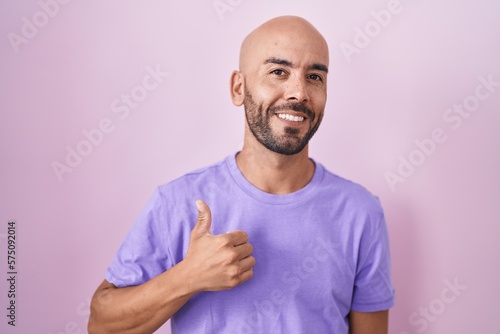Middle age bald man standing over pink background smiling happy and positive, thumb up doing excellent and approval sign
