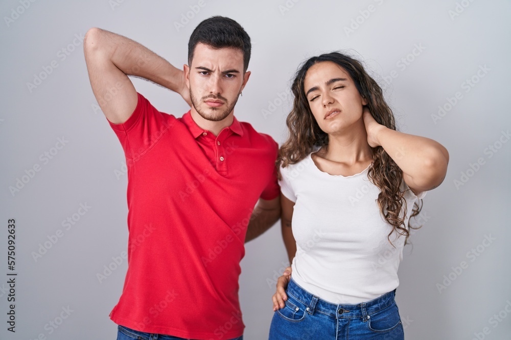 Young hispanic couple standing over isolated background suffering of neck ache injury, touching neck with hand, muscular pain Young hispanic couple standing over isolated background suffering of neck ache injury, touching neck with hand, muscular pain
