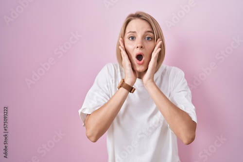 Young caucasian woman standing over pink background afraid and shocked, surprise and amazed expression with hands on face