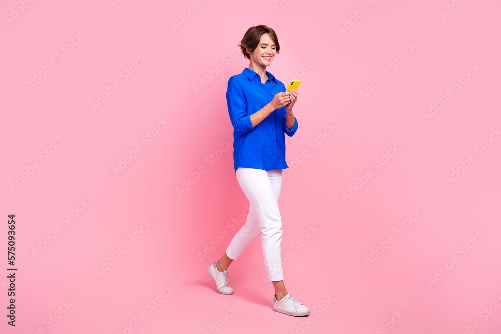 Full length size cadre of young attractive optimistic influencer girl walk hold smartphone chatting online isolated on pink color background Full length size cadre of young attractive optimistic influencer girl walk hold smartphone chatting online isolated on pink color background