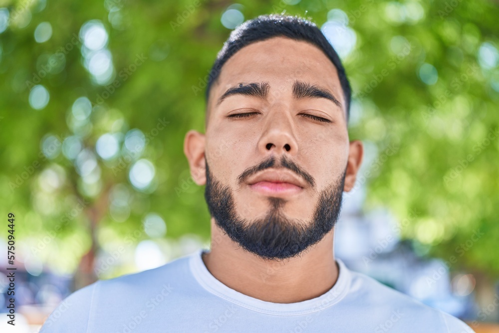 Fototapeta premium Young latin man breathing with closed eyes at park