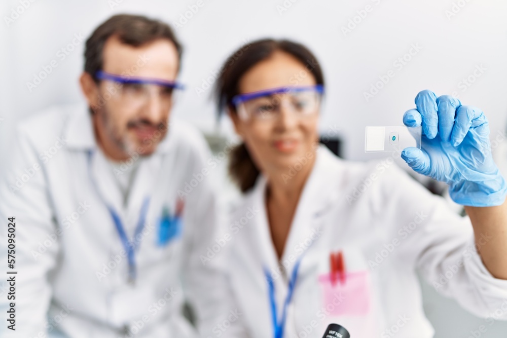 Middle age man and woman partners wearing scientist uniform analyzing sample at laboratory Middle age man and woman partners wearing scientist uniform analyzing sample at laboratory