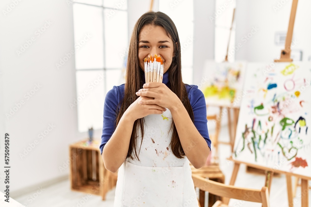 Young latin woman covering mouth with paintbrushes at art studio Young latin woman covering mouth with paintbrushes at art studio