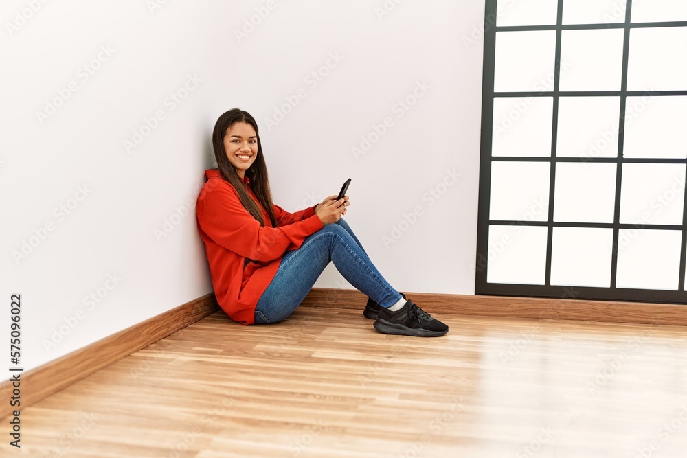 Young latin woman using smartphone sitting on the floor at empty room Young latin woman using smartphone sitting on the floor at empty room