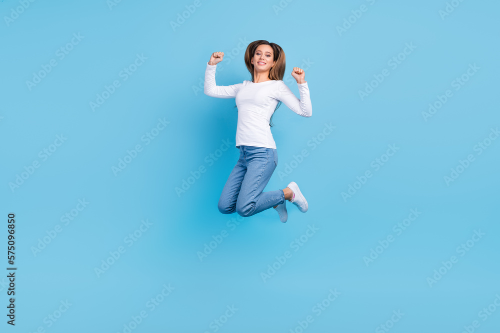 Full length photo of sweet lucky woman wear white shirt jumping high rising fists isolated blue color background