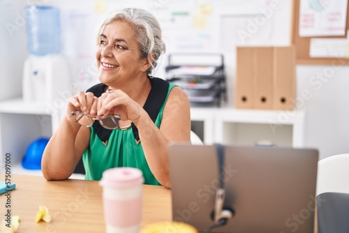 Middle age grey-haired woman business worker smiling confident sitting on table at office