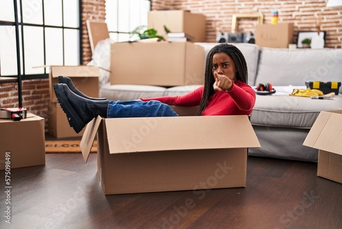 Young african american with braids moving to a new home inside of a cardboard box pointing with finger to the camera and to you, confident gesture looking serious © Krakenimages.com