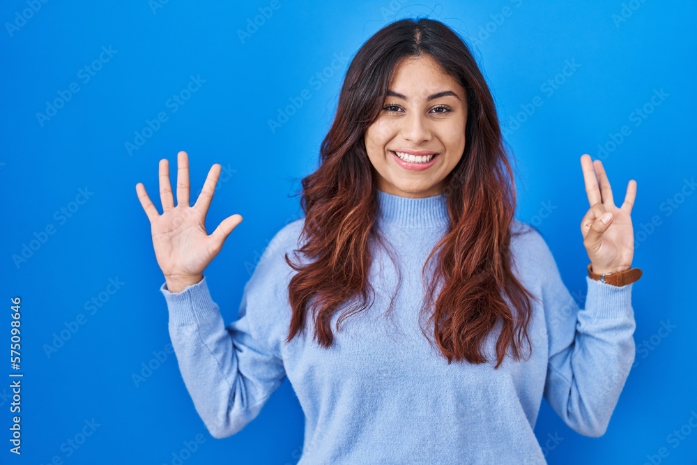 Hispanic young woman standing over blue background showing and pointing up with fingers number eight while smiling confident and happy. Hispanic young woman standing over blue background showing and pointing up with fingers number eight while smiling confident and happy.