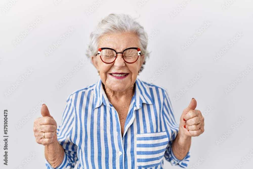 Senior woman with grey hair standing over white background excited for success with arms raised and eyes closed celebrating victory smiling. winner concept. Senior woman with grey hair standing over white background excited for success with arms raised and eyes closed celebrating victory smiling. winner concept.